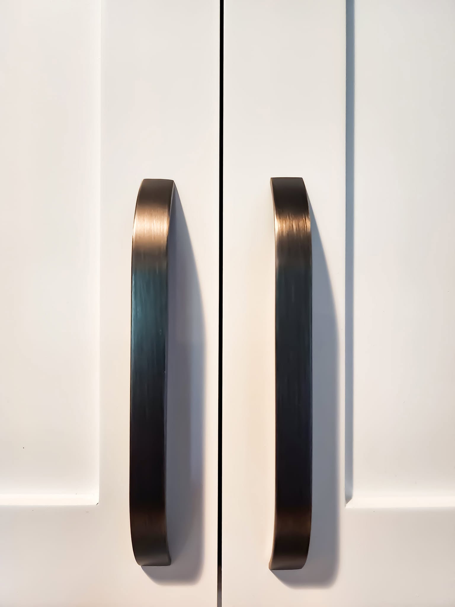 Two oil-rubbed bronze arch-style cabinet pulls on white doors
