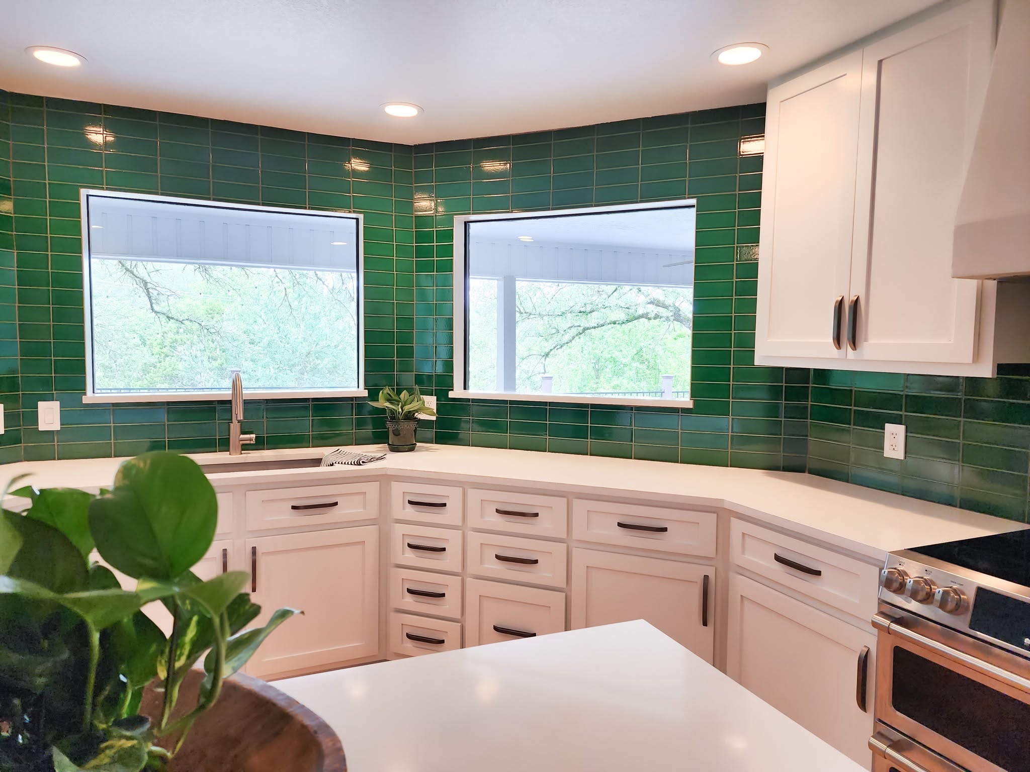 Oil-rubbed bronze bar pulls on white cabinet doors in a green-tiled kitchen